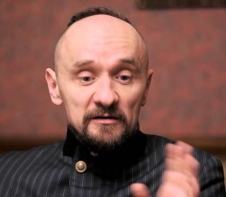 Dynamiczne zdjęcie przedstawiające scenę z jednego ze spektakli Jana Klaty, ukazujące aktorów w ekspresyjnych pozach na tle nowatorskiej scenografii, z dramatycznym oświetleniem.