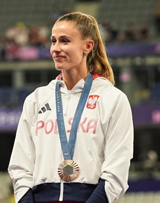 Natalia Bukowiecka uśmiechnięta, trzymająca medal, na tle symbolizującym sukces sportowy.