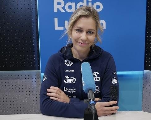 Aleksandra Mirosław, uśmiechnięta, w stroju sportowym, stojąca przed ścianką wspinaczkową, symbolizująca rolę ambasadorki wspinaczki.